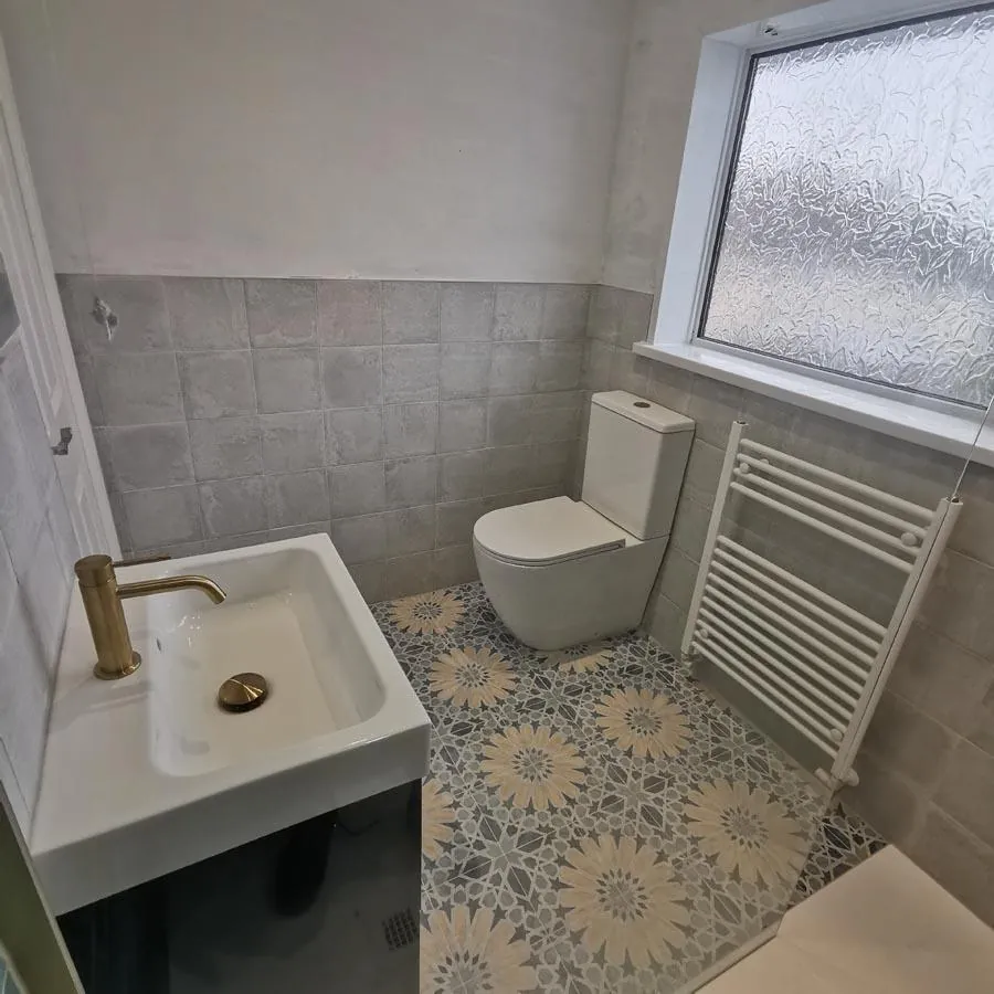 Bathroom with patterned floor tiles, a brass basin tap and white towel radiator